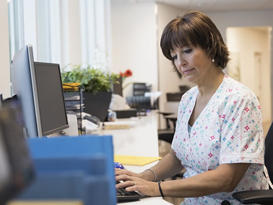 Female nurse typing at computer at clinic nurses station