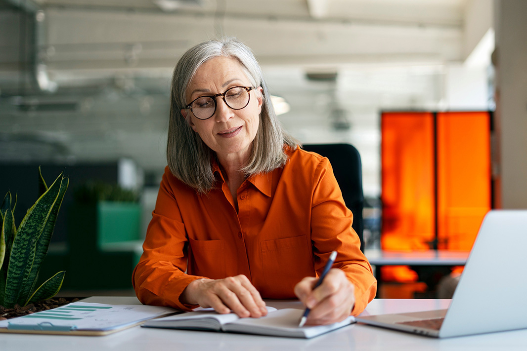 Confident mature woman, writer using laptop computer, taking notes