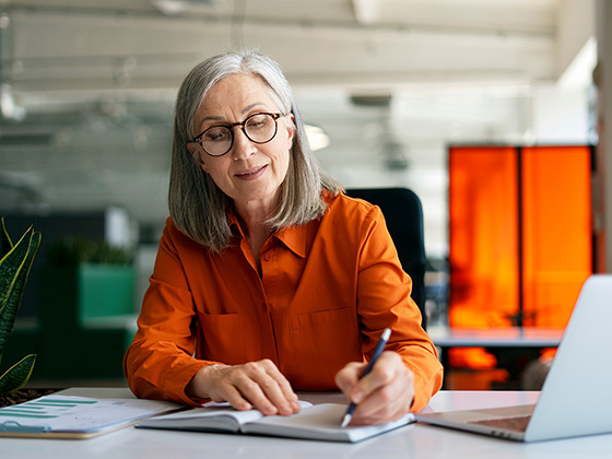 Confident mature woman, writer using laptop computer, taking notes
